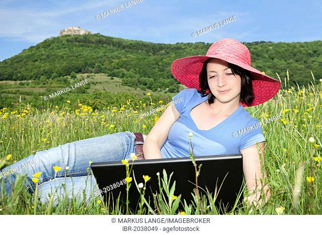 Young woman wearing a red hat using a laptop in a meadow