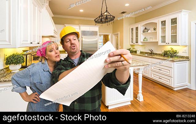 Male contractor in hard hat discussing plans with woman in custom kitchen interior