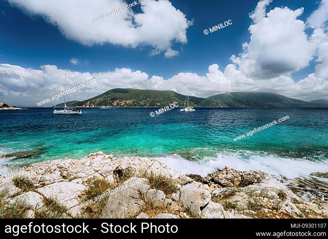 Crystal clear transparent blue turquoise teal Mediterranean sea water in Fiskardo town. White yacht in open sea at anchor under amazing white clouds, Kefalonia
