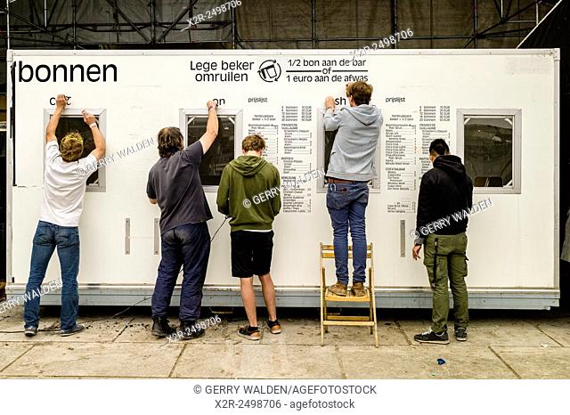 People removing a pricelist from the side of a portacabin at the end of a music festival (Ghent, Belgium). The sign reads 'Empty cup exchange'