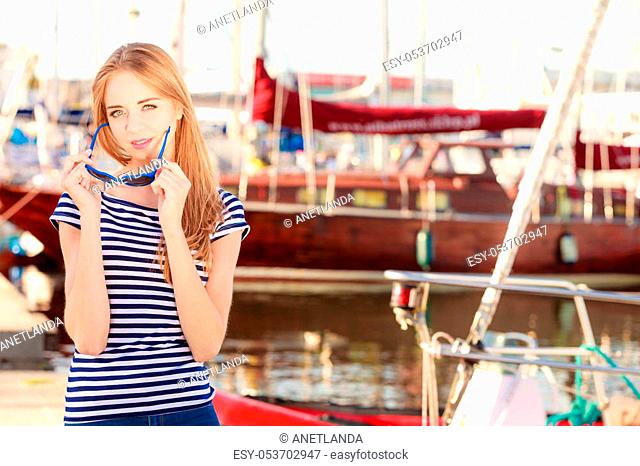 Travel tourism and people concept. Fashion blonde girl with blue heart shaped sunglasses in marina against yachts in port