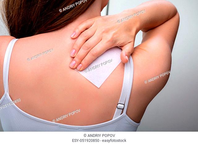 Rear View Of Woman Sticking Patch To Help With Stiff Neck