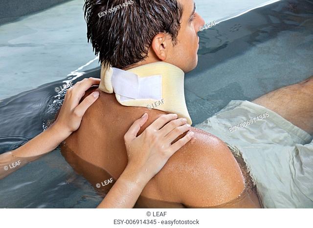 Young man wearing neck brace being massaged by female while sitting in pool