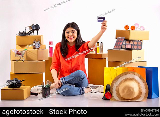 A young woman showing her credit card sitting amidst shopping items in the background