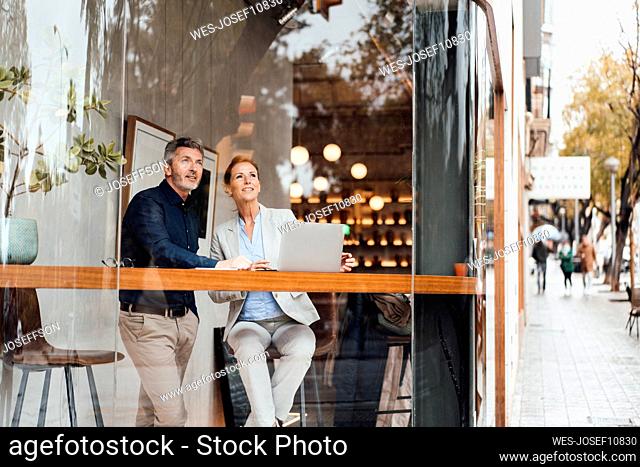 Businessman with businesswoman in cafe seen through glass window