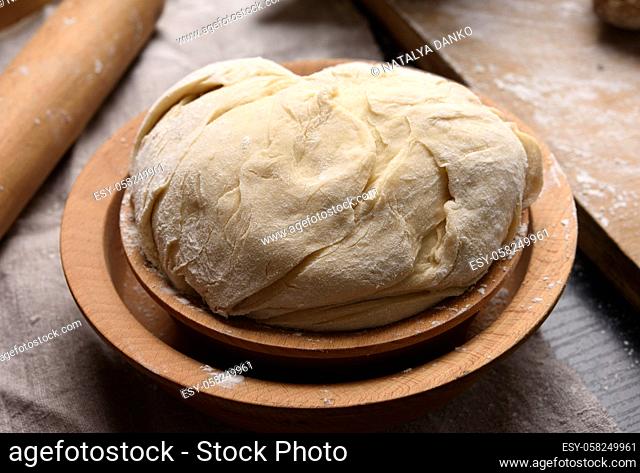 kneaded dough made of white wheat flour in a wooden plate, close up