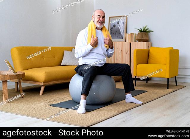 Senior man with napkin around neck sitting on fitness ball at home