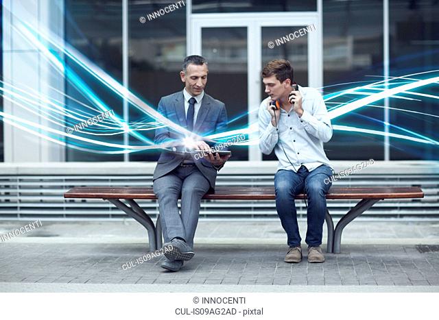 Businessman and young man watching digital tablet and waves of illumination
