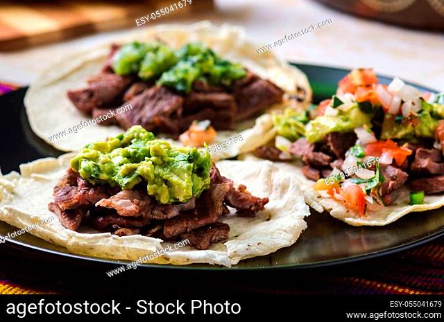 Mexican carne asada tacos, literally grilled meat tacos. These are chopped barbecued beef served on soft corn totillas with salsa verde and pico de gallo