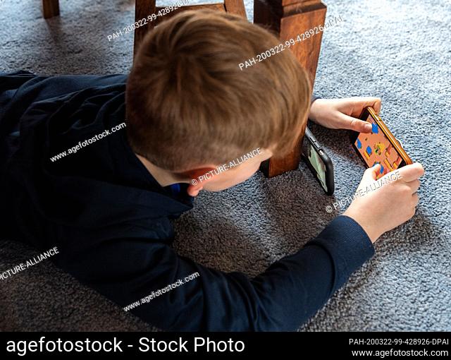 20 March 2020, Saxony, Dresden: A boy plays a video game on his smartphone and uses a second mobile phone to transfer it to his friend via Facetime