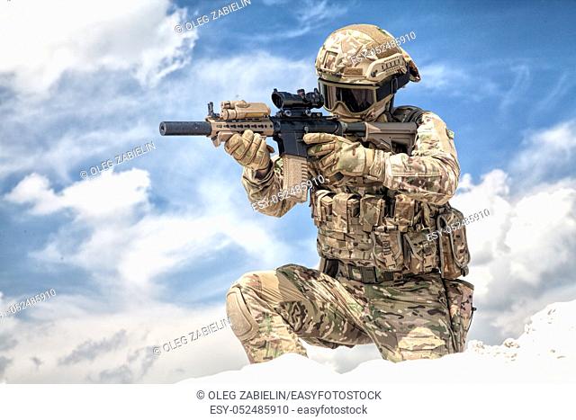 Fully equipped with tactical ammunition airsoft player in military camouflage uniform, aiming with optical sight on service assault rifle replica while stand on...
