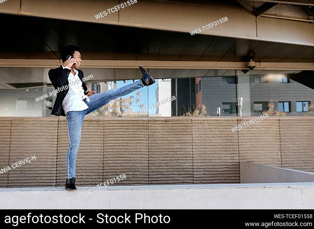 Flexible businessman talking through smart phone while standing on retaining wall