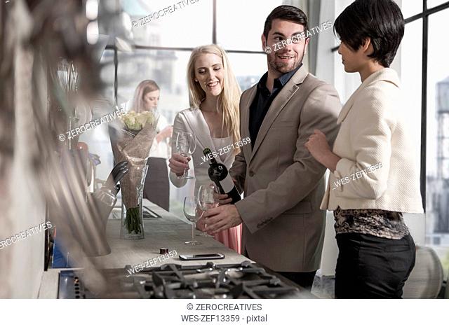 Man with female friends and wine bottle in kitchen