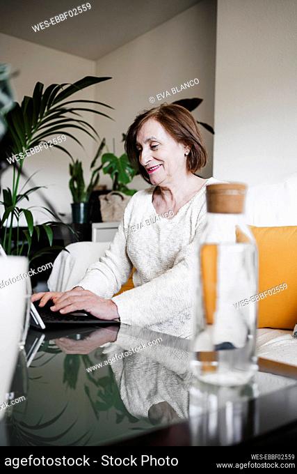Smiling senior woman using laptop while sitting at table In living room