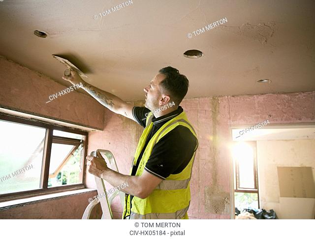 Construction worker plastering ceiling in house