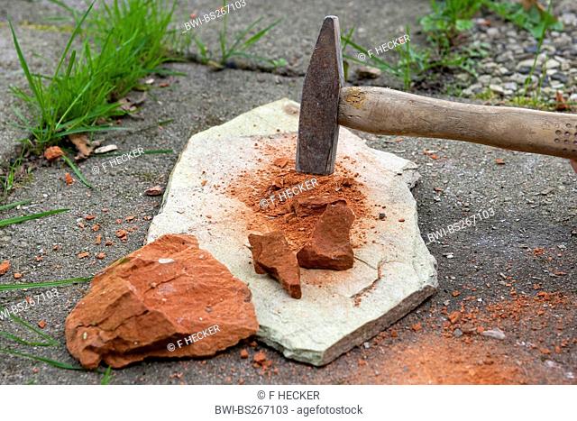 crushing a red sandstone with a hammer to paint with earth colour, Germany