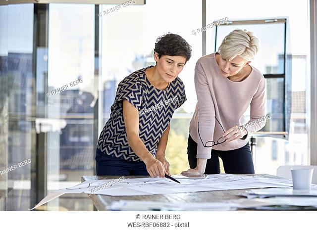 Two businesswomen discussing floor plan on desk in office