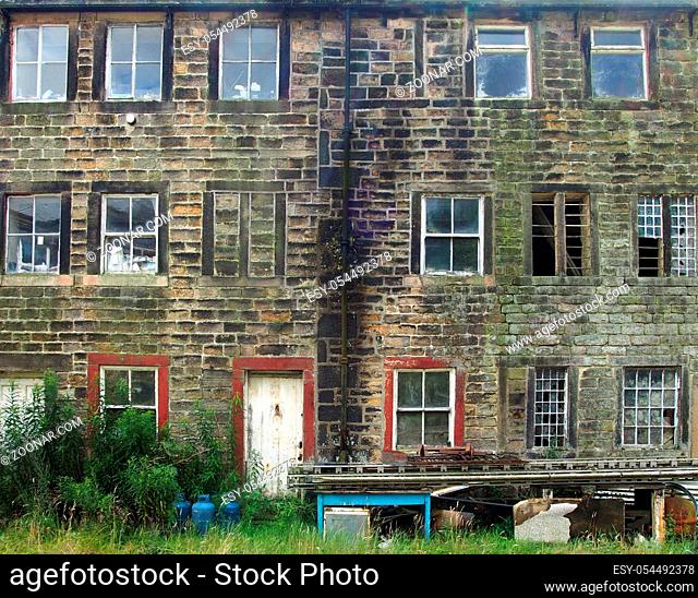 the facade of old derelict stone houses with broken windows and peeling red door with junk outside the front
