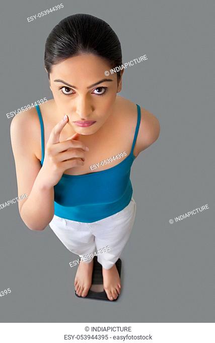 Portrait of worried young woman standing on weighing scale isolated over gray background