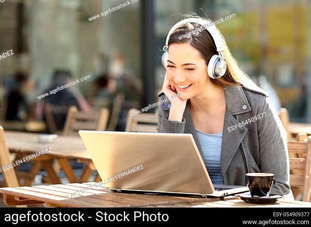 Happy woman watching media content on laptop with headphones on a restaurant terrace