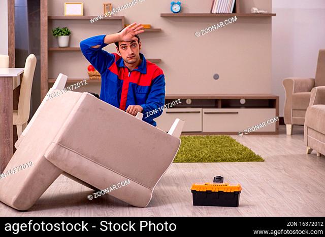 Young contractor repairing arm-chair indoors