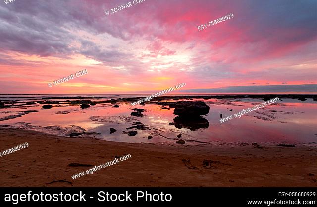 Morning colours of the sunrise paint the sky and reflect in the tidal water. Space for copy. Location: Bateau Bay Australia