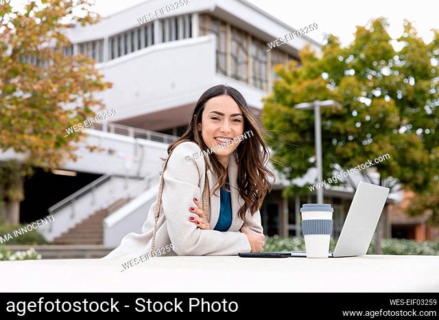Happy businesswoman with disposable coffee cup and laptop in park