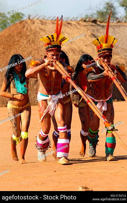 Two native indios with two young girls in festive clothing and feathres in their hair playing their long pipe, Mato Grosso, Brazil, South America
