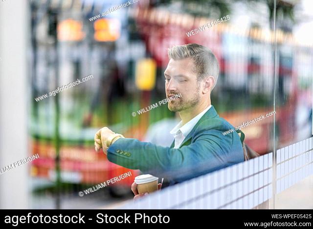 Young businessman checking time on wristwatch seen through glass