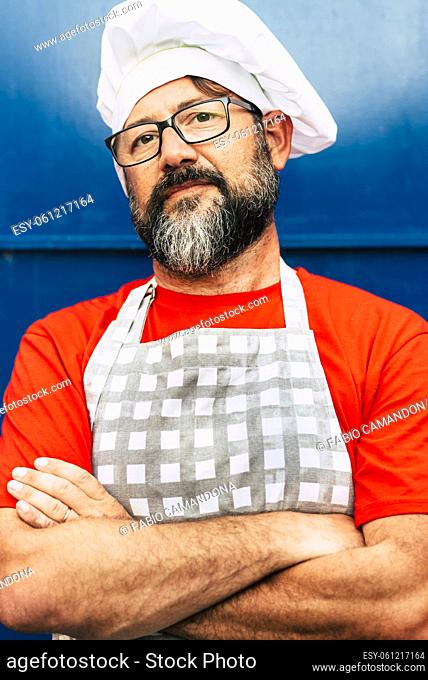 Portrait of adult chef hipster bearded man looking on camera and wear white hat - concept of restaurant or cafe and people working on it - glasses and red blue...