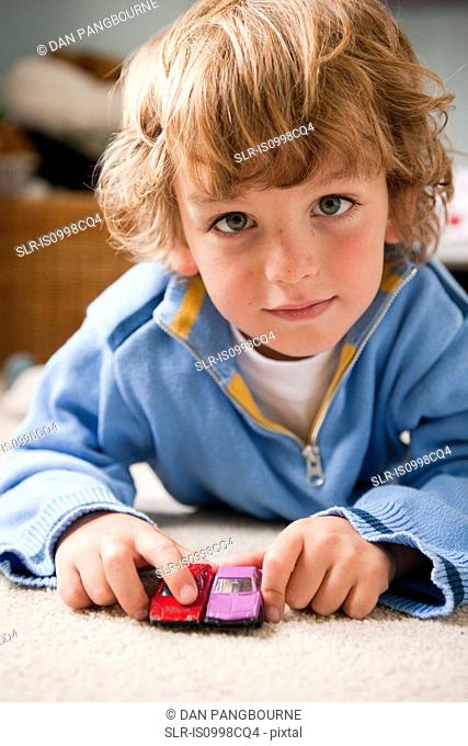 Young boy playing at home with two toy cars