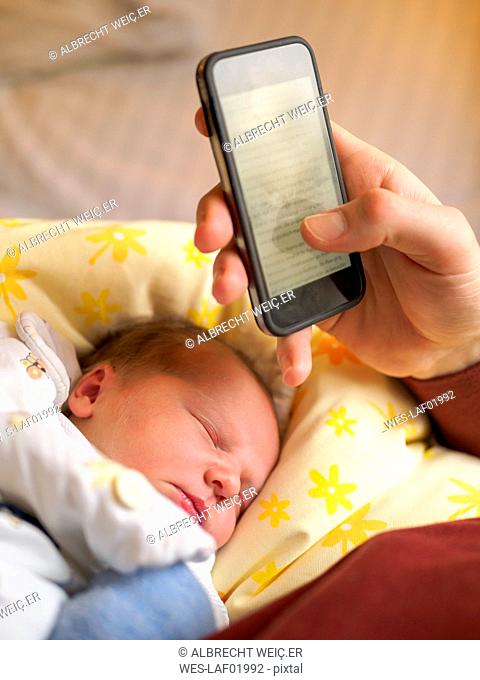 Father using smartphone, newborn girl sleeping