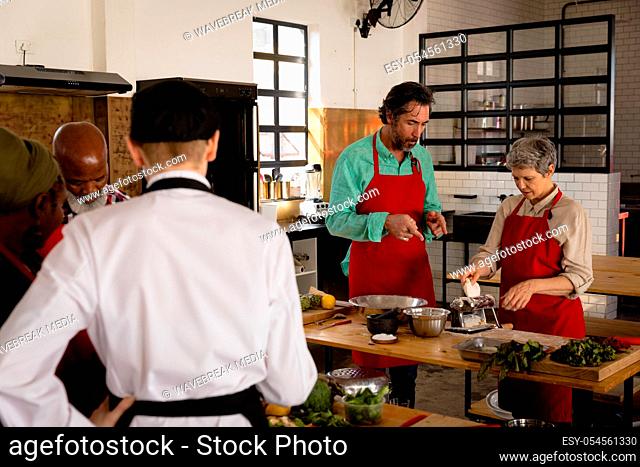 Front view of a multi-ethnic group of Senior adults at a cookery class, the diverse adult students listening to instructions from a Caucasian female chef...