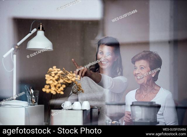 Smiling woman pointing by grandmother seen through glass window