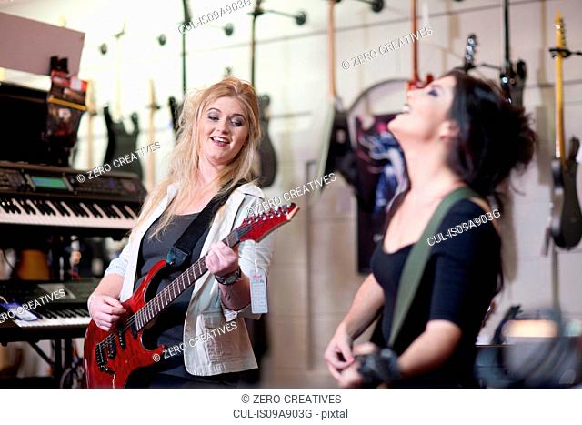Two young women trying electric guitars in music store