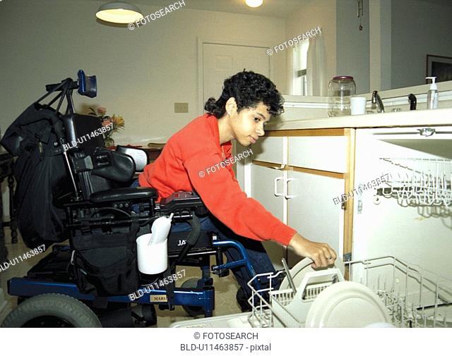 Woman with a disability, utilizing a wheelchair for mobility, unloading her dishwasher in her apartment
