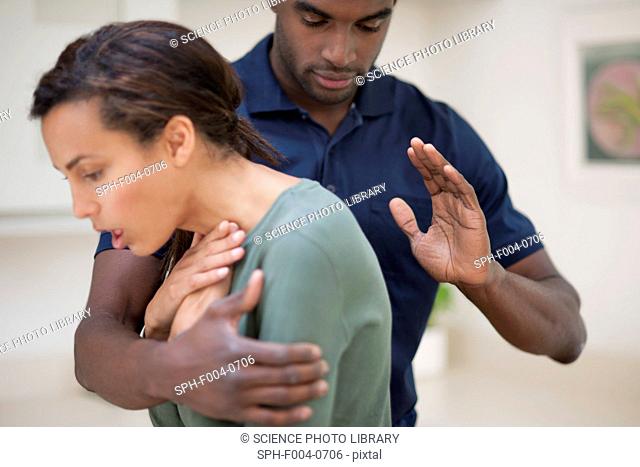 Woman choking. The man is trying to dislodge the foreign object by hitting her between the shoulder blades