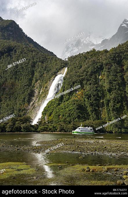 Tourist boat in the fjord, Bowen Falls waterfall, Milford Sound, Fiordland National Park, Te Anau, Southland, South Island, New Zealand, Oceania