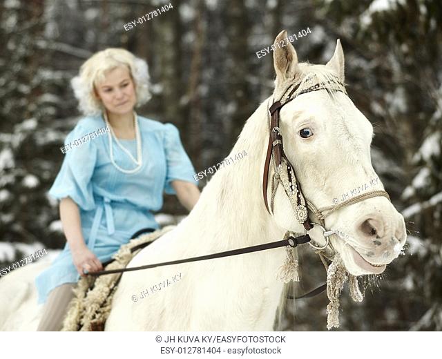 Attractive woman wearing blue dress and she riding a white horse, focus on horse eyes. South Finland in February