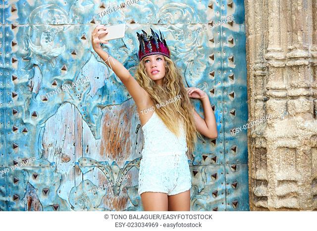 Blond teen girl tourist in Mediterranean old town door with colorful feathers on hair