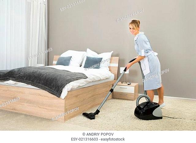 Female Housekeeper Cleaning Rug With Vacuum Cleaner In Hotel Room