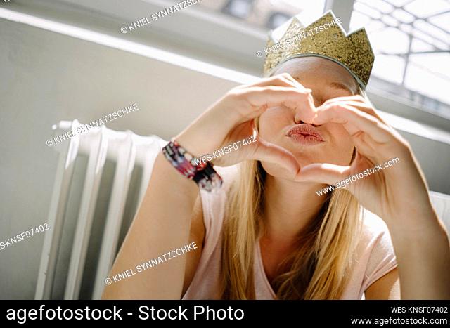 Young woman wearing a crown shaping a heart with her hands