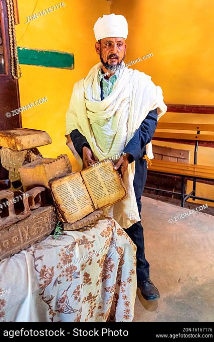 Yeha, Tigray Region, Ethiopia - April 28, 2019: Orthodox priest shows a painted holy bible in amharic langugage from the 14th century in Great Temple of the...