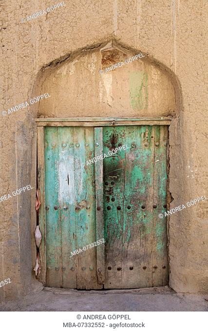 Oman, Al Hamra, green wooden door with arch at mud facade