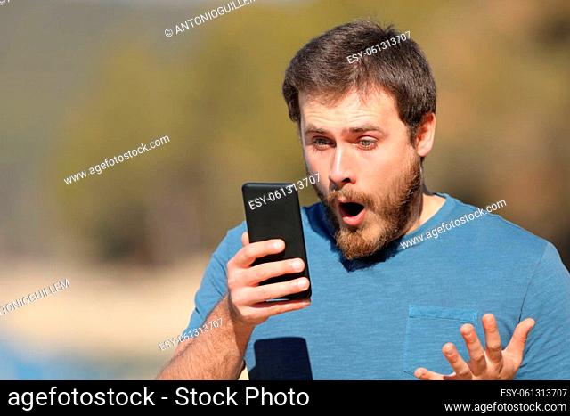 Surprised man checking smart phone content standing outside in a lake