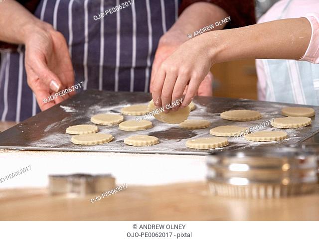 Woman and young girl in kitchen putting cut out dough onto a baking sheet