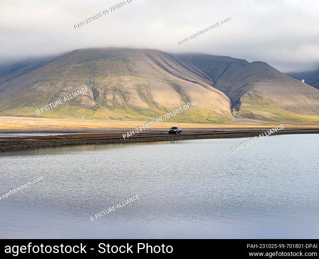 22 August 2023, Norway, Longyearbyen: A car drives along the shore of a shallow lake against the backdrop of mountains. Photo: Soeren Stache/dpa