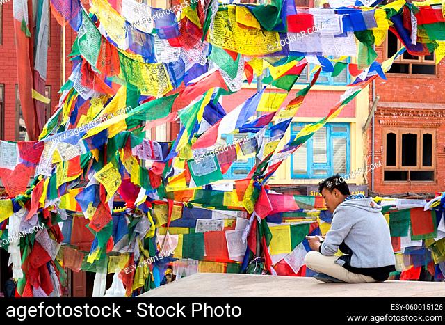 Kathmandu, Nepal - December 3, 2014: Nepalese man sitting under colorful prayer flags at the historic Boudhanath Stupa