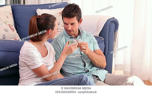 Happy couple sitting floor drinking wine together