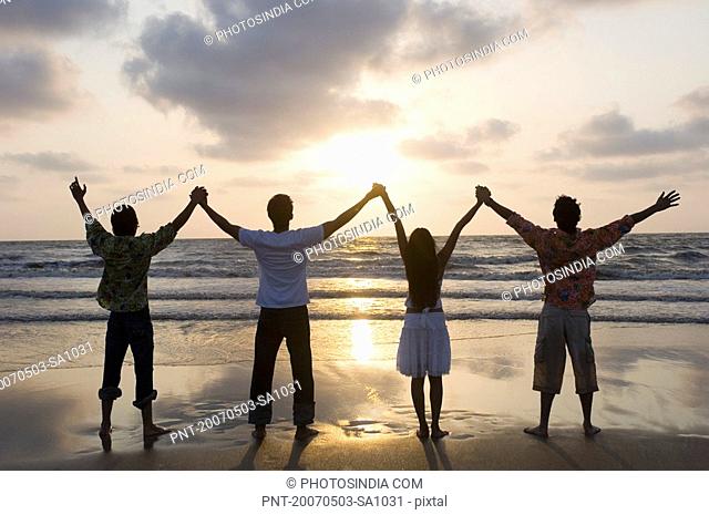 Rear view of three young men and a young woman standing side by side with holding hands on the beach